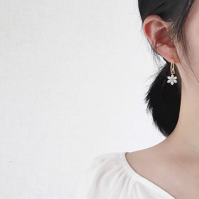 A woman wearing gold hoop earrings with a CZ flower charm.