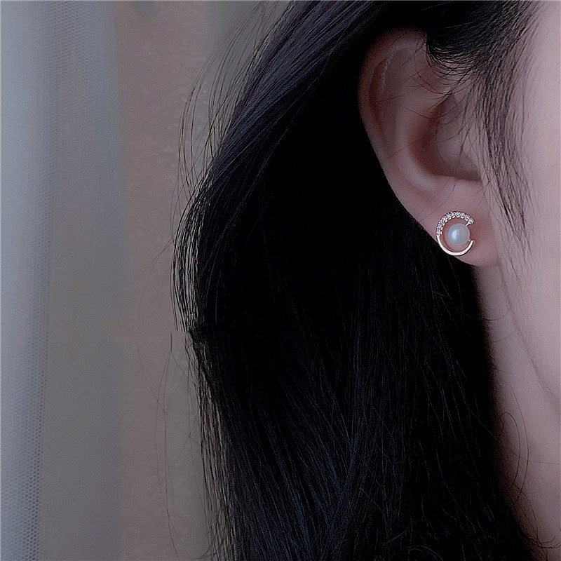 A model wearing gold CZ and pearl stud earrings.