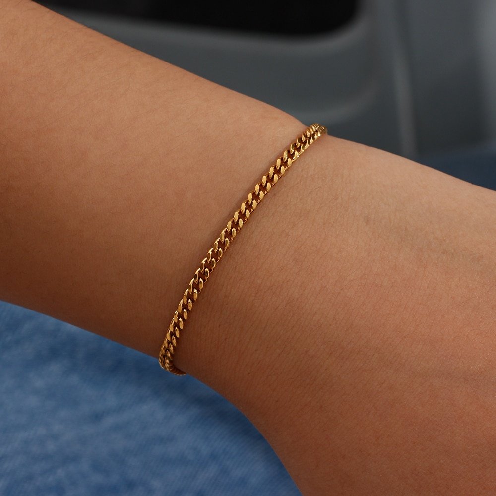 A model wearing a thin gold chain bracelet.