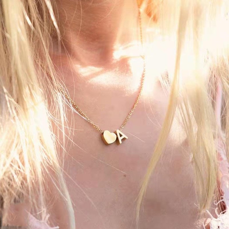 A woman wearing a gold initial necklace with a heart charm.
