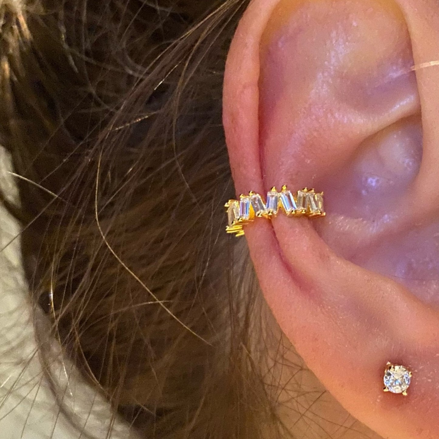A woman wearing a gold ear cuff with CZ baguette stones.