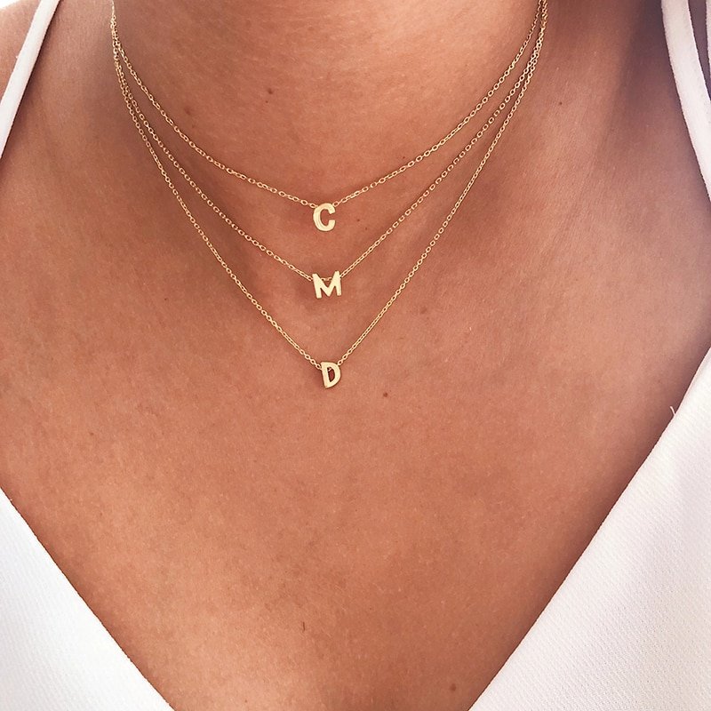 A model wearing three gold initial layering necklaces.