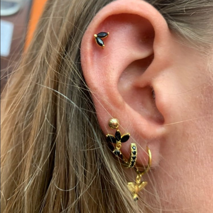 A woman wearing gold stud earrings with black CZ stones.
