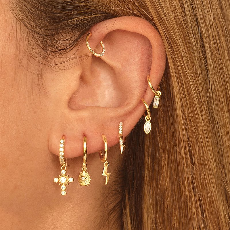 A model wearing multiple charm huggie earrings.
