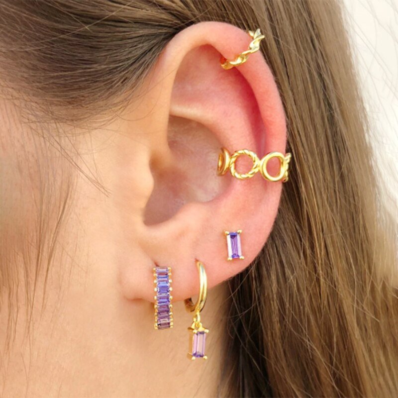 A model wearing multiple gold earrings with purple stones.