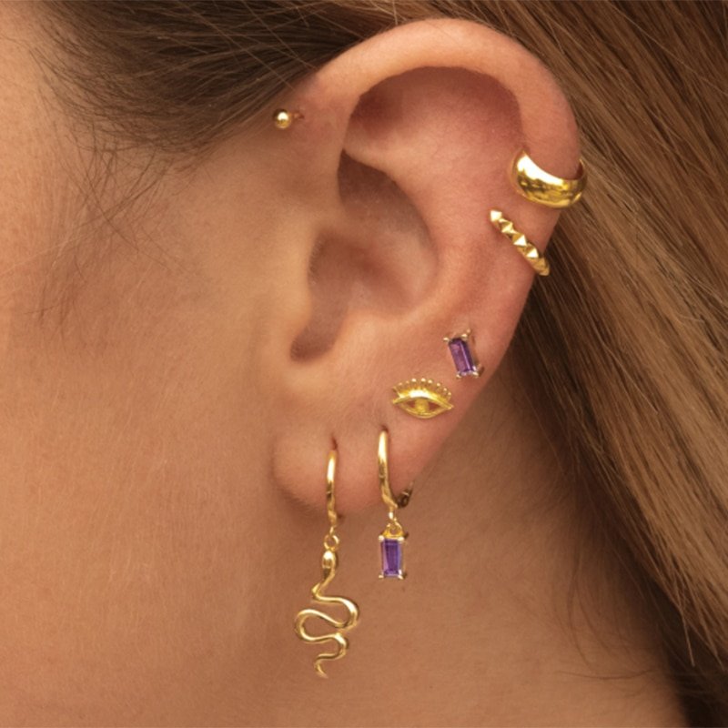 A model wearing multiple gold ear piercings with purple CZ stones.