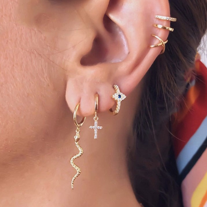 A model wearing snake, cross, and evil eye earrings.