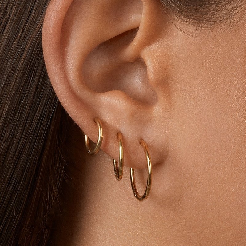 A model wearing three sizes of gold hoop earrings.
