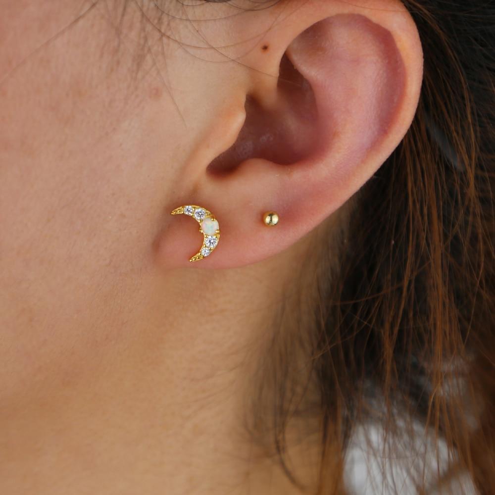 A woman wearing gold crescent moon studs with opals. 