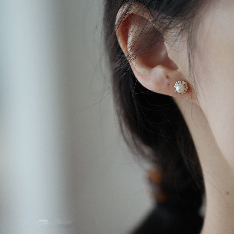A model wearing tiny pearl stud earrings with a halo of CZ stones.