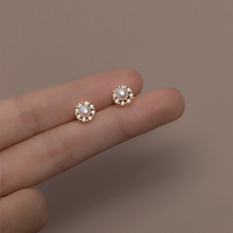 A woman holding a pair of gold Pearl CZ Halo Studs.