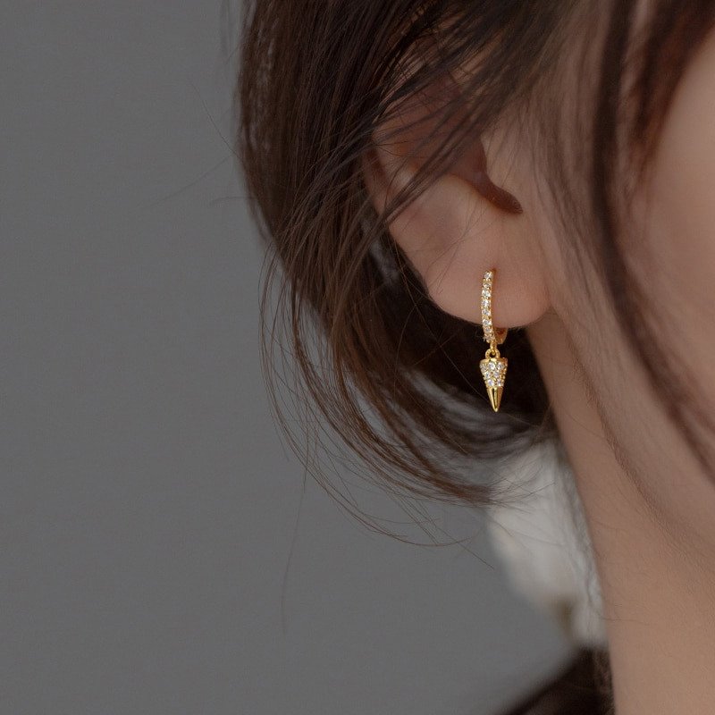 A woman wearing gold spike huggie hoop earrings.