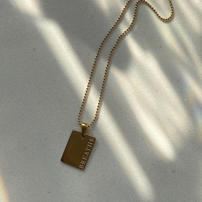 Gold dog tag necklace engraved with "Breathe".