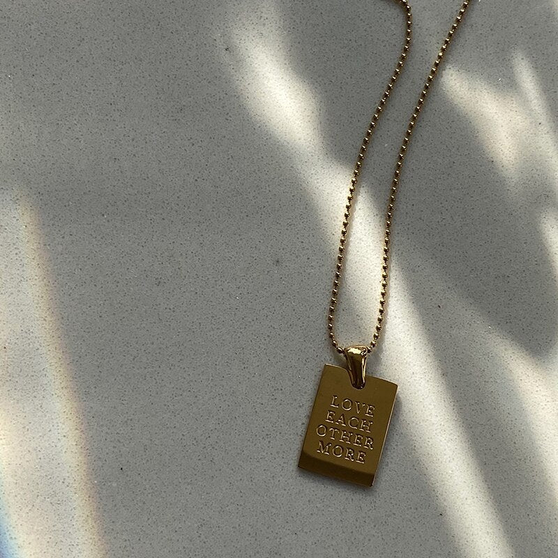 Gold dog tag necklace with "Love Each Other More" engraved on it.