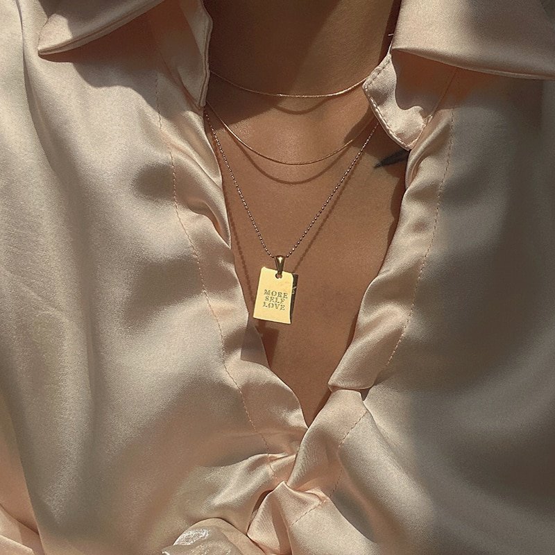 A model wearing a gold dog tag necklace.