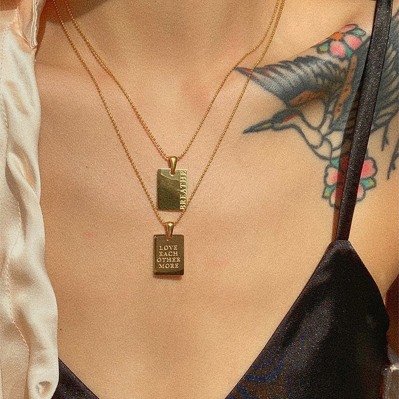 A model wearing two gold dog tag necklaces.