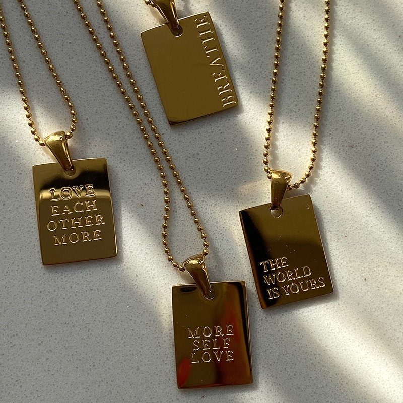 Four gold dog tag necklaces with positive messages engraved.