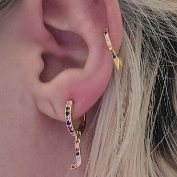 A woman wearing multiple gold hoops with rainbow CZ stones.