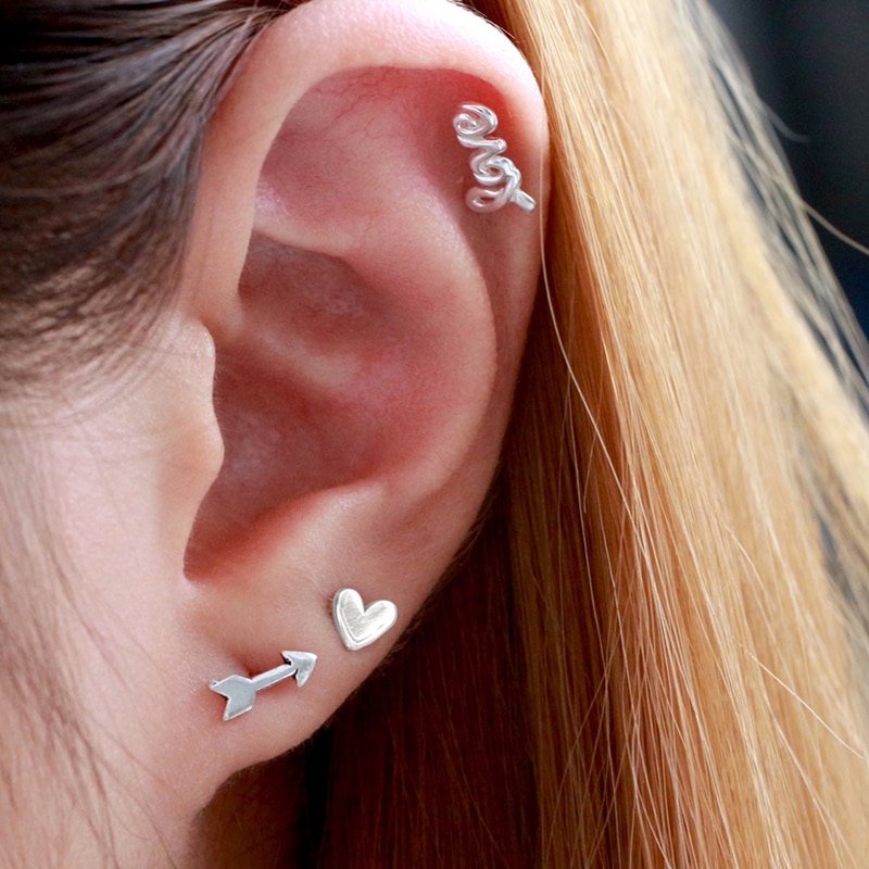 A model wearing silver heart, arrow and love stud earrings.