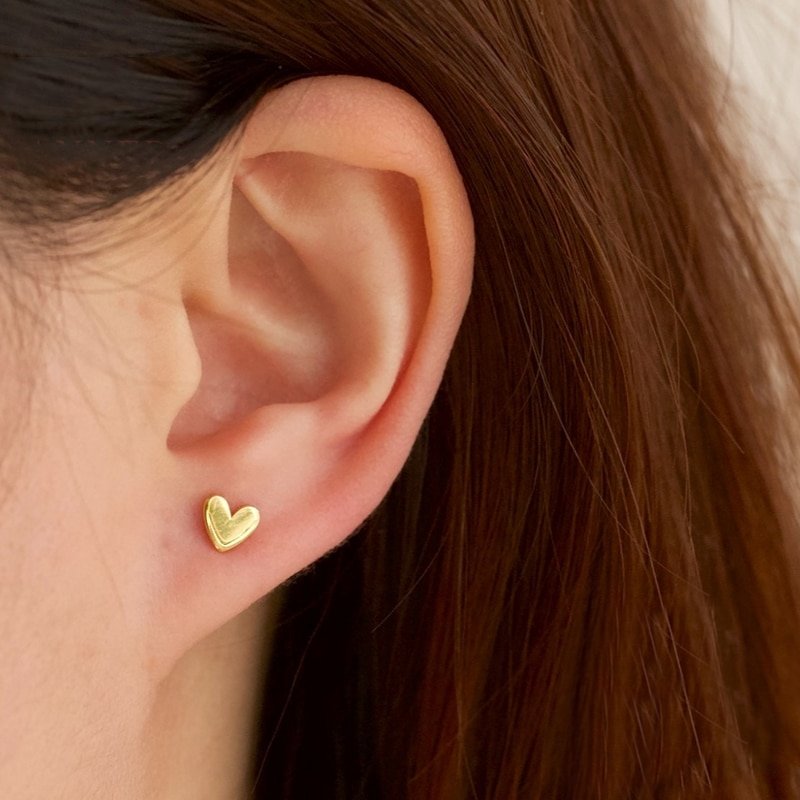 A model wearing tiny gold heart stud earrings.