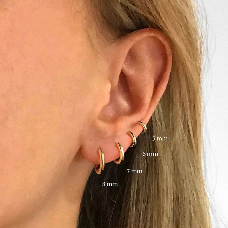 A model wearing four different sizes of huggie hoop earrings.