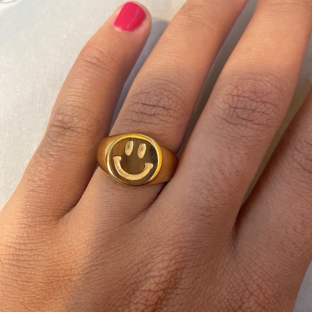 A woman wearing a chunky gold ring with a smiley face.