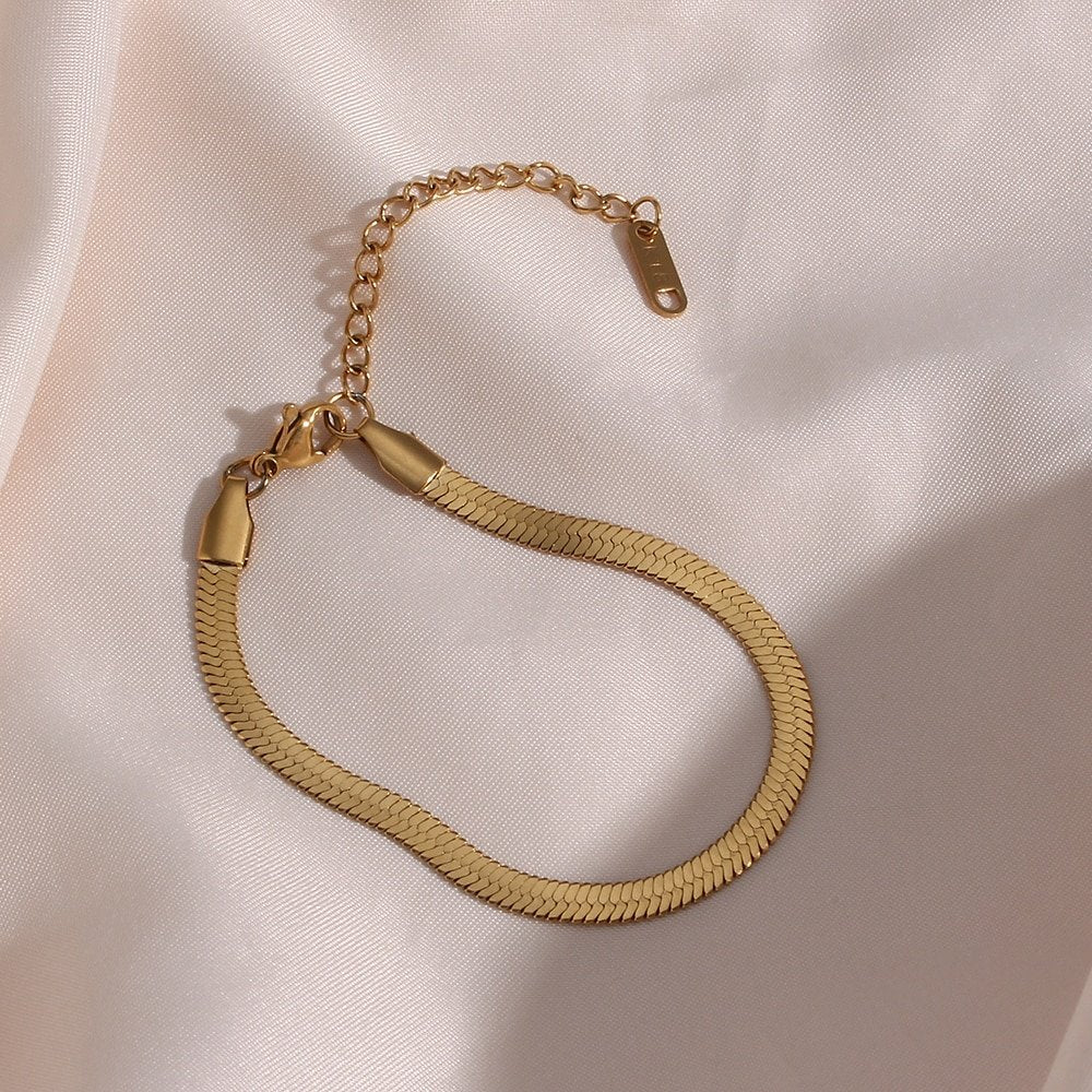 Gold snake chain bracelet on a pink silk cloth.