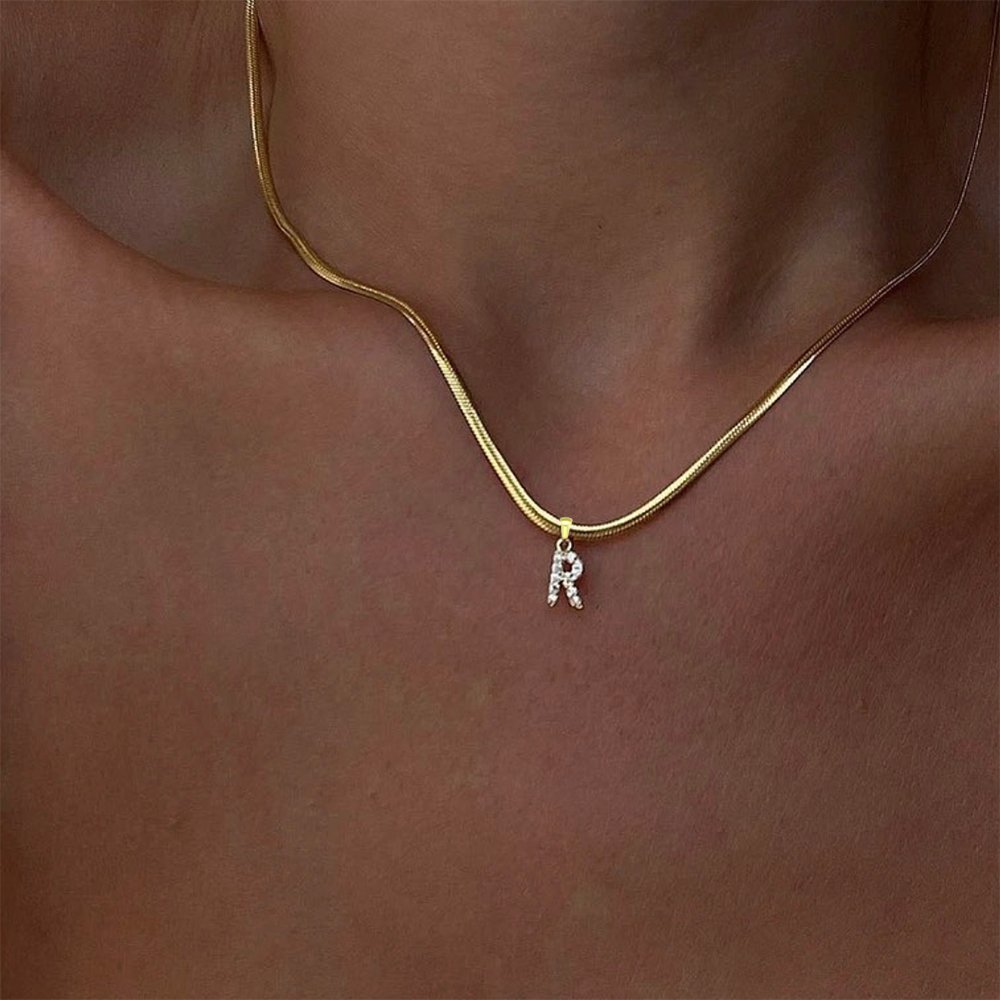 A model wearing a gold snake chain initial necklace.
