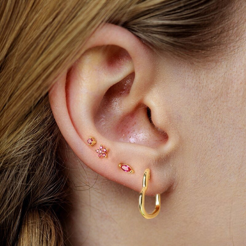 A model wearing gold earrings with pink sones.