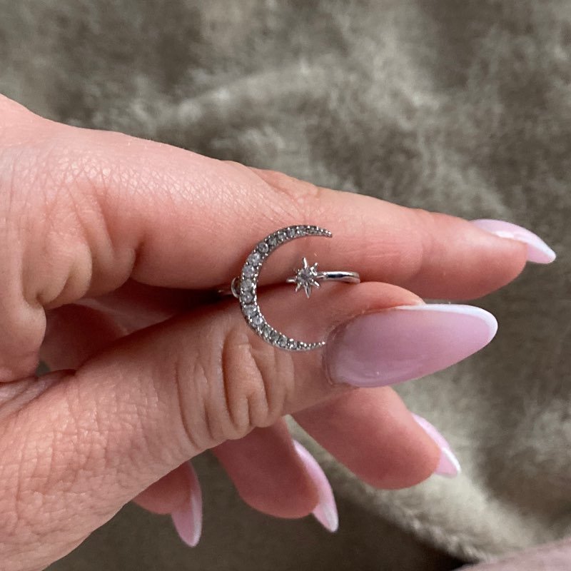 A woman's hand with pink nails holding the Star Crescent Moon Ring.