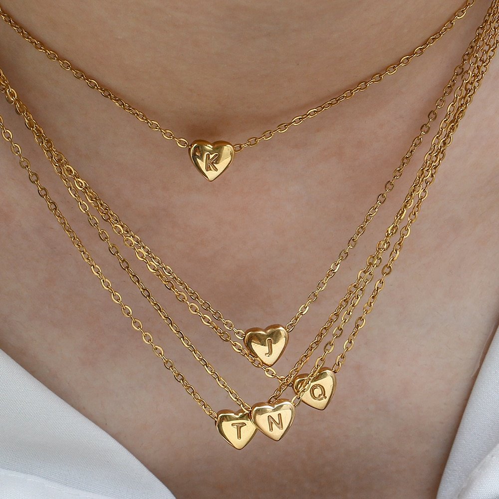 A woman wearing a bunch of tiny heart initial necklaces.