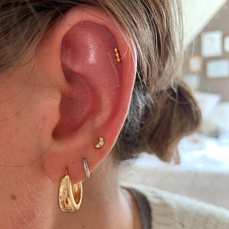 A woman wearing a tiny gold moon cartilage piercing.