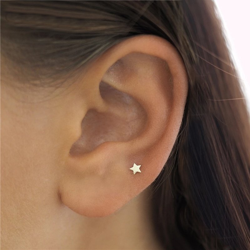 A model wearing tiny gold star stud earrings.