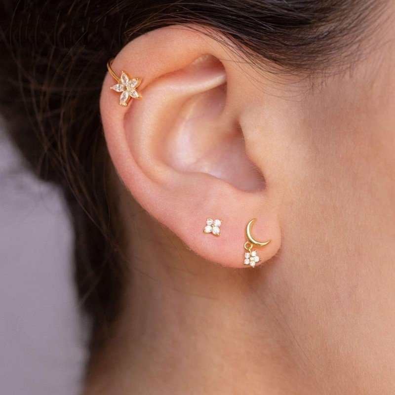 A model wearing multiple gold flower earrings.