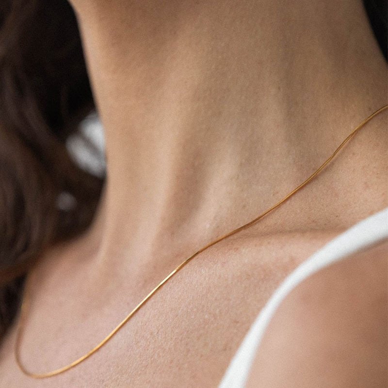 A model wearing a thin snake chain gold necklace.